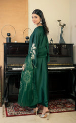 Woman in a green embroidered outfit standing in front of a piano