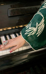 Hand playing a piano with a green embroidered sleeve