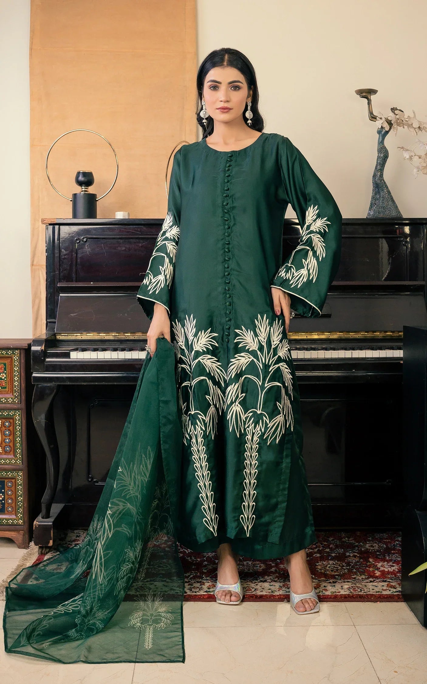 Woman in a green embroidered outfit standing in front of a piano