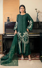 Woman in a green embroidered outfit standing in front of a piano